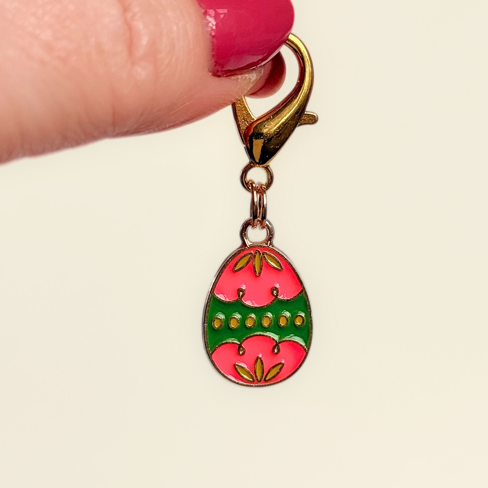 Colourful pink and green patterned Easter egg enamel dog collar charm that easily attaches to collars and harnesses with a gold plated lobster clasp. Pictured being held up against a cream background.￼