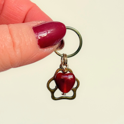 Crystal for dogs pet collar charm featuring a 10mm red carnelian heart shaped bead and a brass gold coloured paw print tag. A stone for confidence, vitality and motivation. Pictured being held up.
