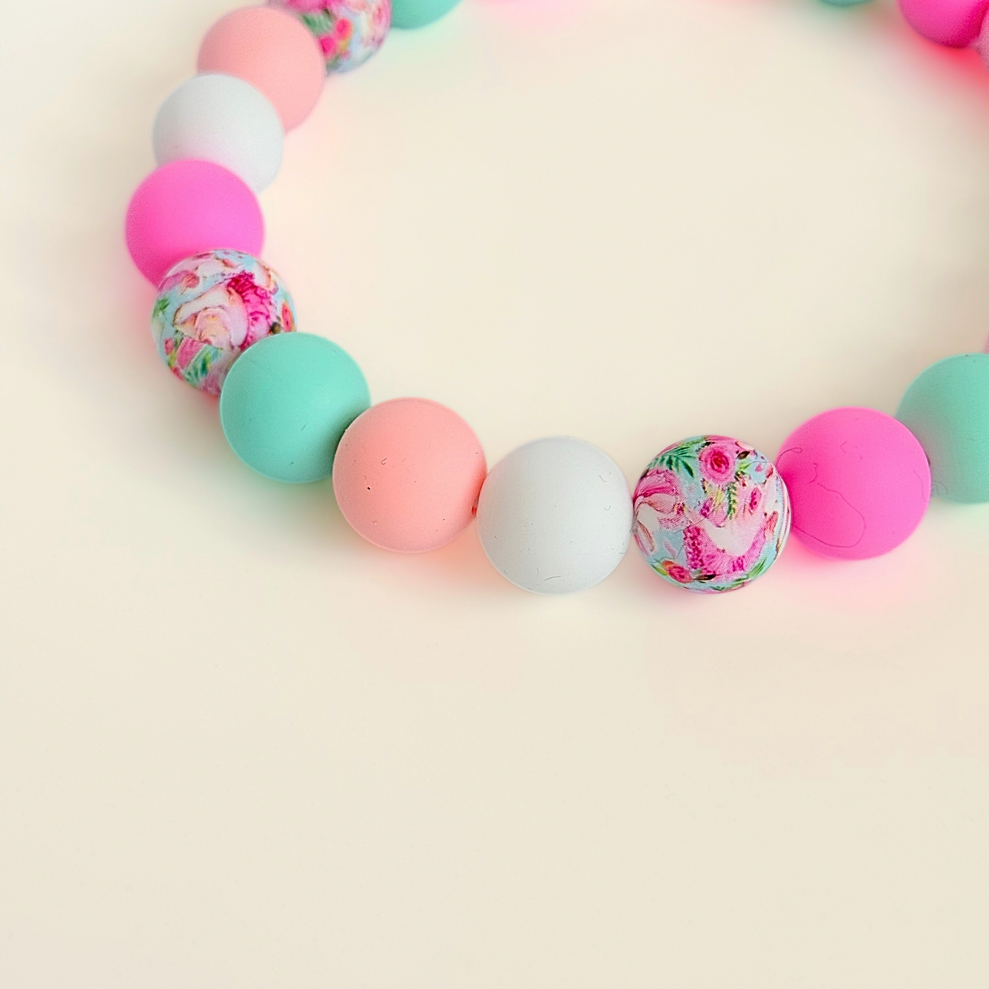 Silicone beaded dog necklace made with 15mm round beads in pink, green, white and a floral flowers print. On a strong, elastic stretch cord. Pictured close up.￼