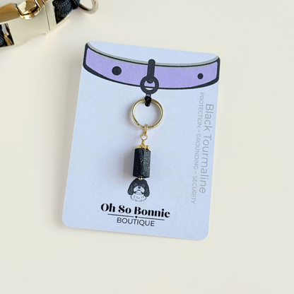 Crystal dog collar charm featuring a raw black tourmaline natural bead with gold plated accents. Featuring a brass split ring for easy attaching to your pet’s collar. Pictured on the display card, next to a black paracord dog collar.