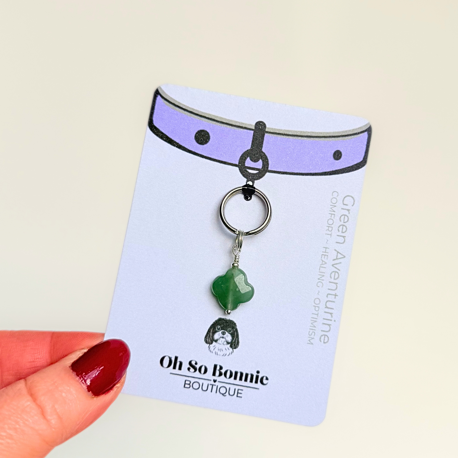Green aventurine four leaf clover shaped crystal dog collar charm. Crystals for dogs, gemstone for optimism, healing and comfort. Pictured against a cream background, on the display card.