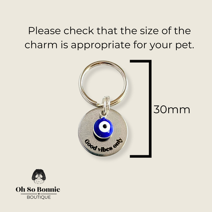 Silver plated brass and stainless steel 15mm dog collar charm with ID tag. Personalised custom identification tag with a small, blue Turkish Evil Eye charm, on a 15mm silver split ring. Engraved with the words ‘Good vibes only’ on the front. Pictured against a cream background showing the dimensions of the charm.