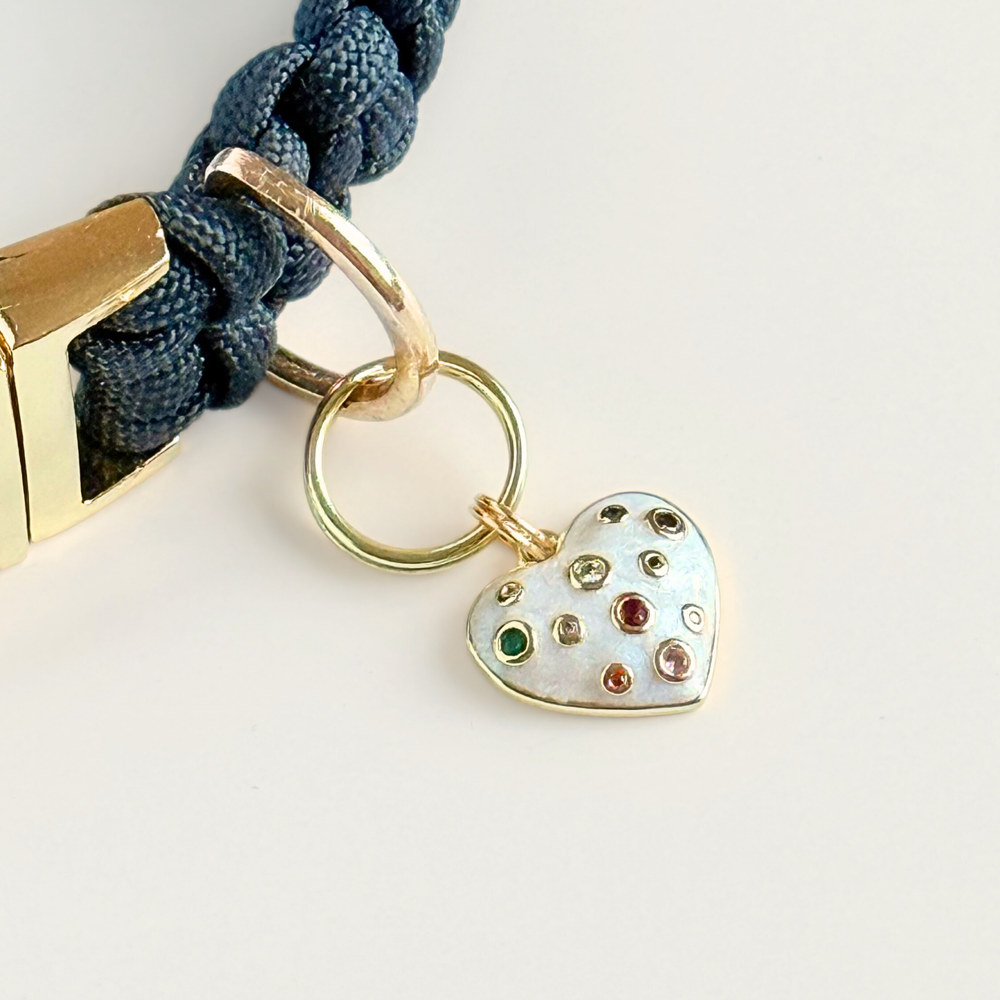Heart-shaped cream / off-white pearlescent coloured enamel and brass dog collar charm featuring a selection of multicoloured cubic zirconia stones. Pictured attached to a black paracord dog collar.