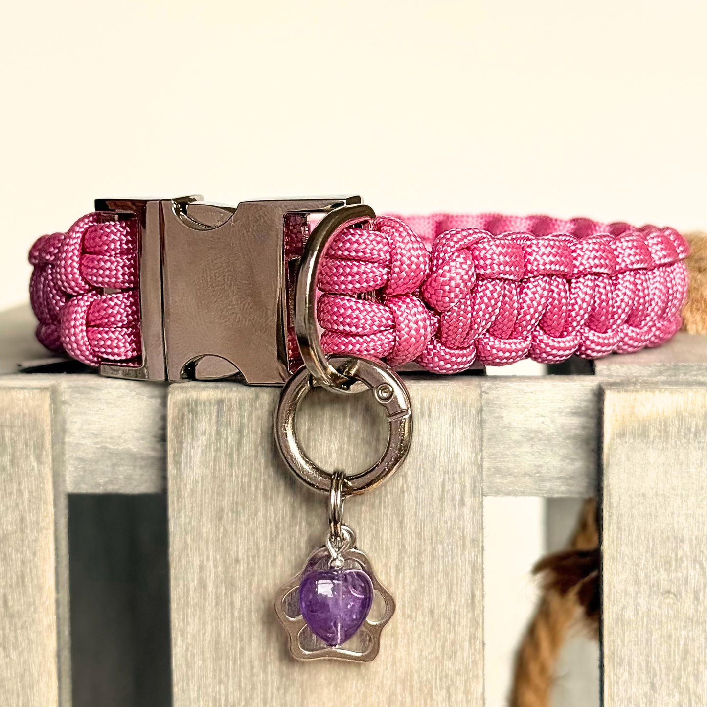 Crystal for dogs pet collar charm featuring a 10mm purple amethyst heart shaped bead and a brass silver coloured paw print tag. Pictured attached to a pink paracord dog collar.