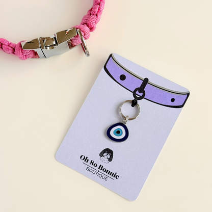Silver plated blue turkish evil eye dog collar charm, for protection, security and grounding, 35mm easy to attach to pet collars. Picture shows the tag on it's display card, next to a pink paracord dog collar.