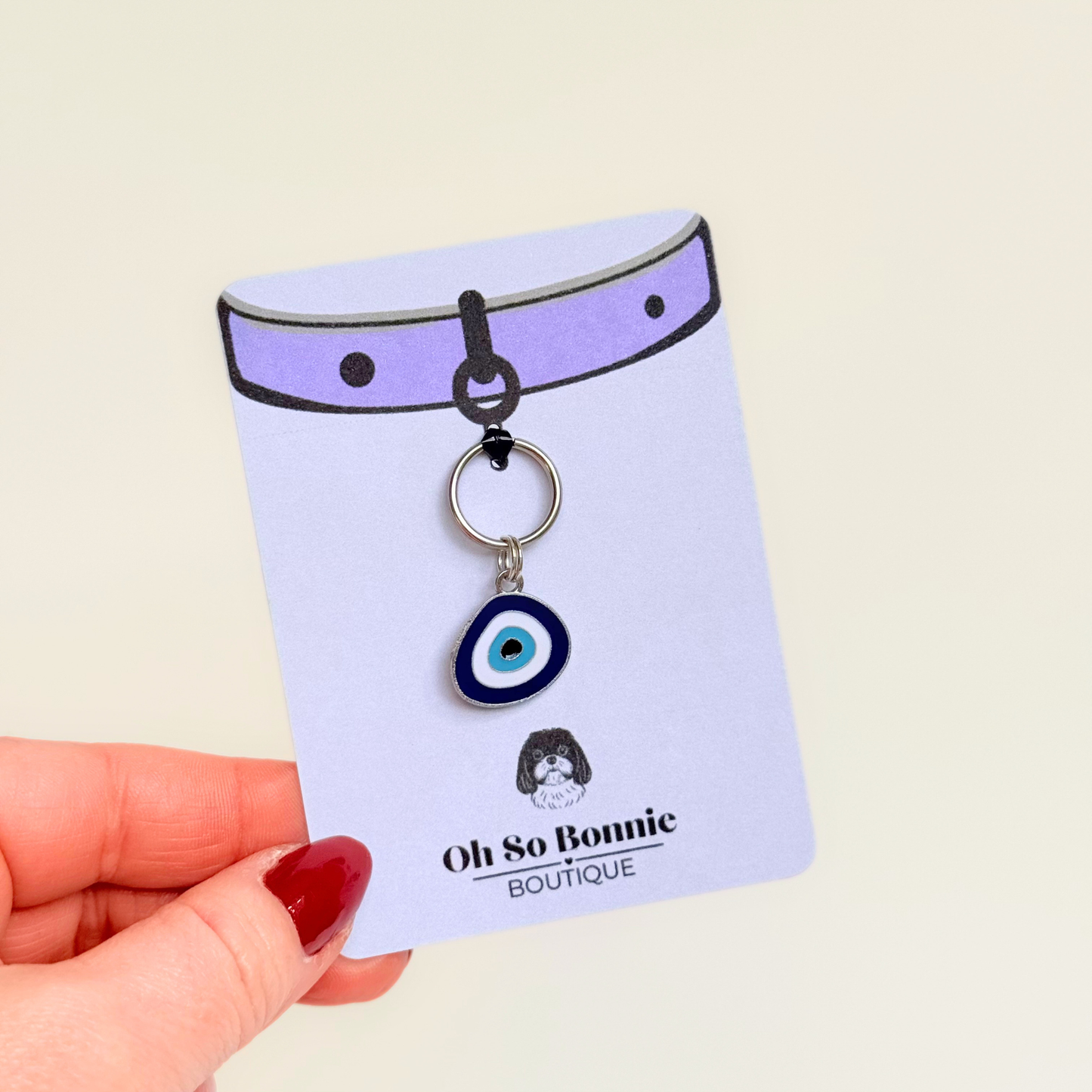 Silver plated blue turkish evil eye dog collar charm, for protection, security and grounding, 35mm easy to attach to pet collars. Picture shows the tag on the display card, being held up.