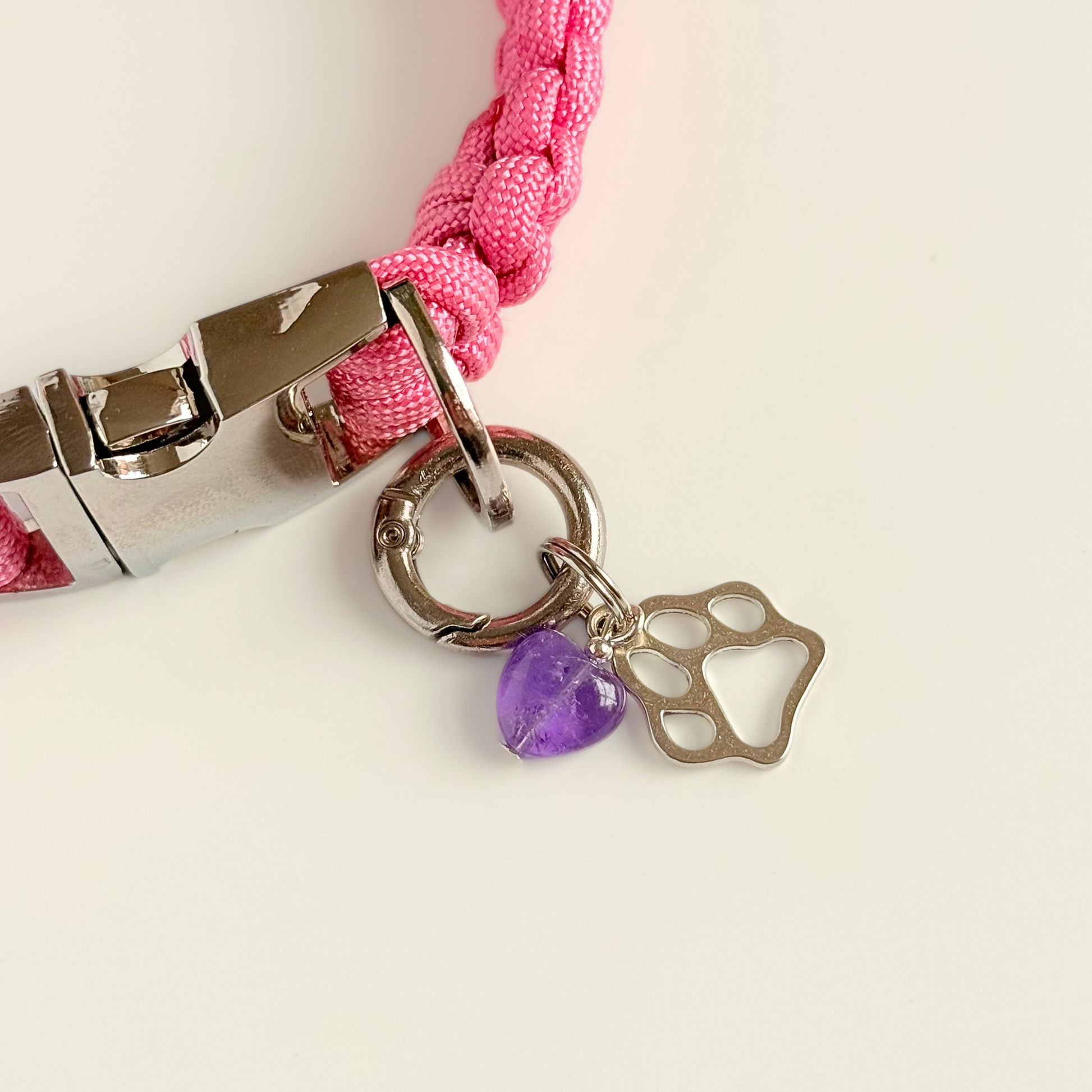 Crystal for dogs pet collar charm featuring a 10mm purple amethyst heart shaped bead and a brass silver coloured paw print tag. Pictured attached to a pink paracord collar.