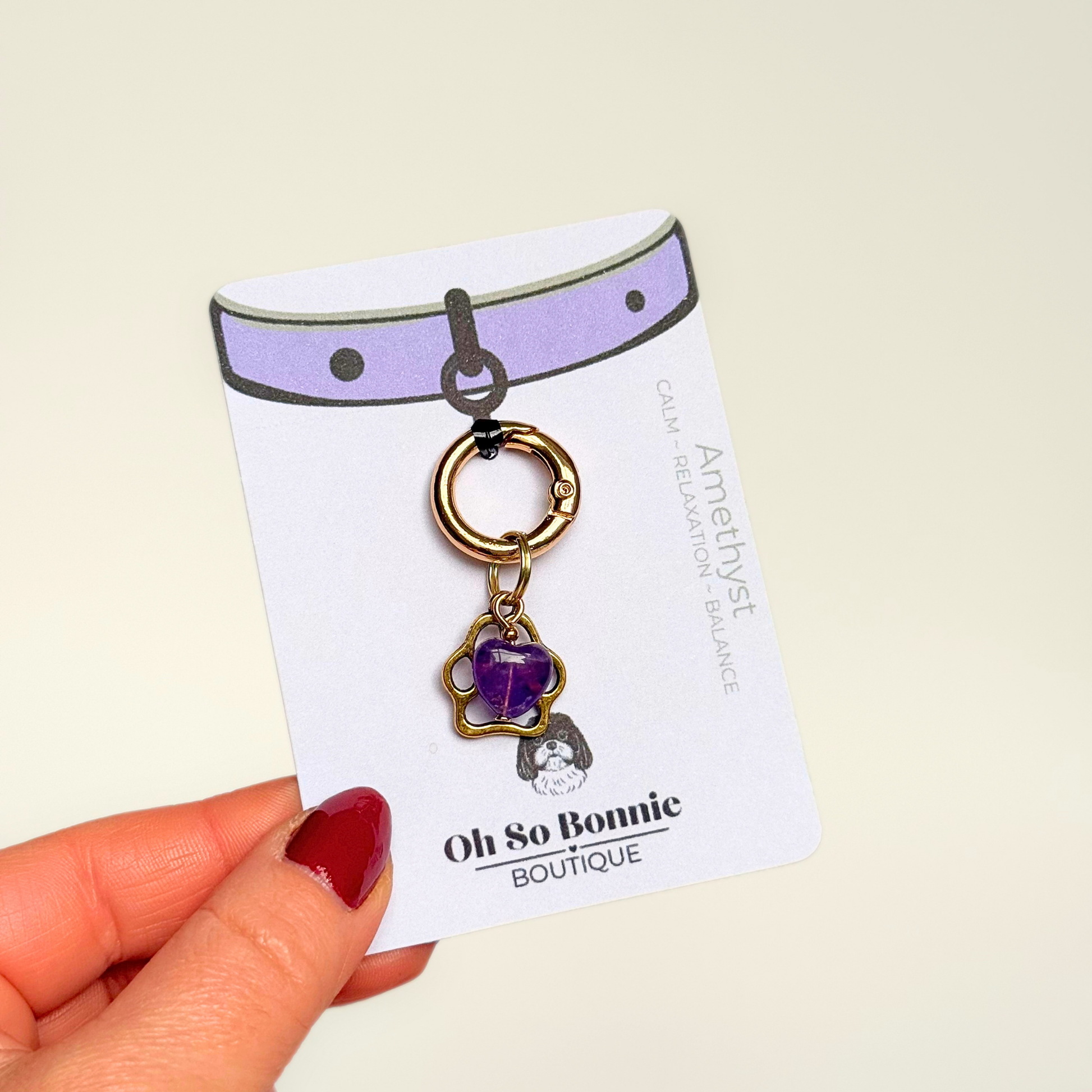Crystal for dogs pet collar charm featuring a 10mm purple amethyst heart shaped bead and a brass gold coloured paw print tag. Pictured on the display card.