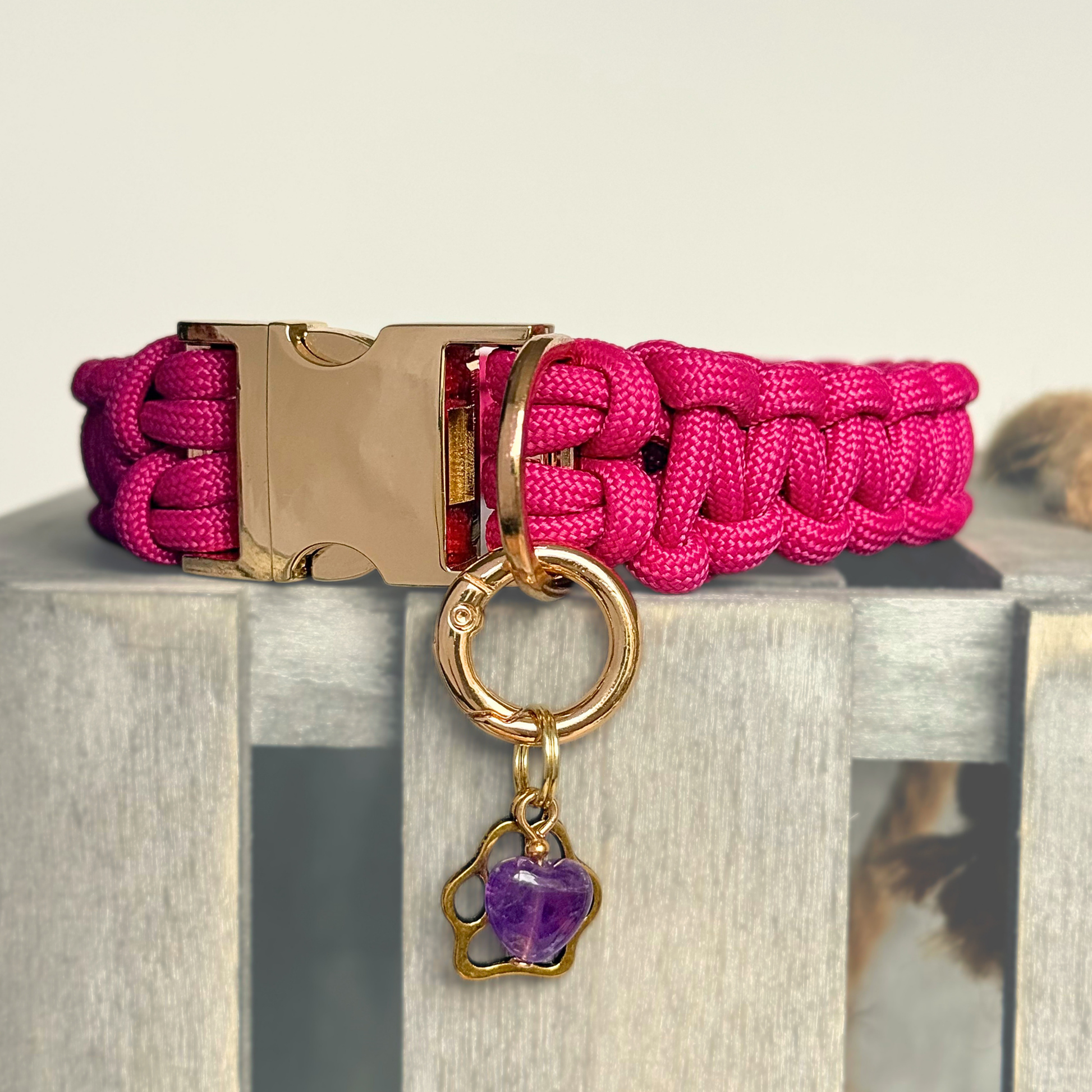 Crystal for dogs pet collar charm featuring a 10mm purple amethyst heart shaped bead and a brass gold coloured paw print tag. Pictured attached to a pink paracord dog collar.