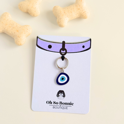 Silver plated blue turkish evil eye dog collar charm, for protection, security and grounding, 35mm easy to attach to pet collars. Picture shows the tag on the display card, next to some dog biscuits.