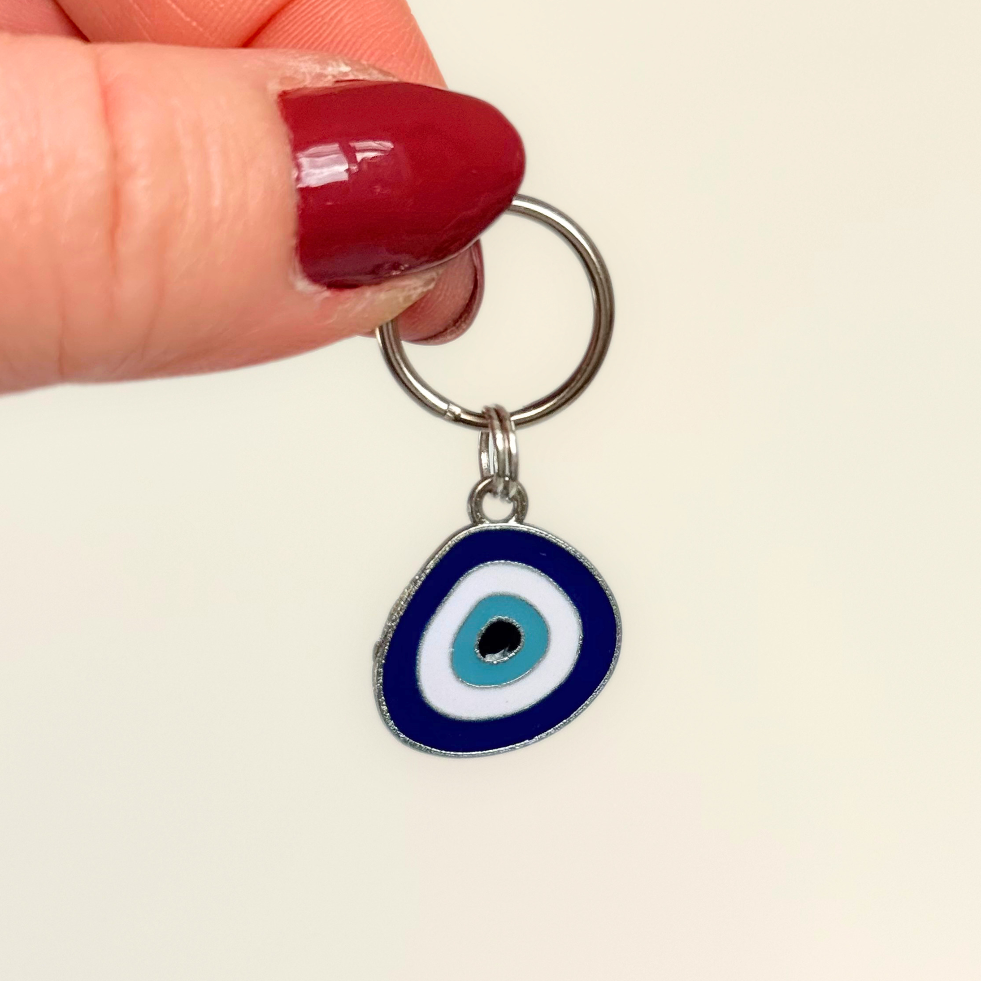Silver plated blue turkish evil eye dog collar charm, for protection, security and grounding, 35mm easy to attach to pet collars. Picture shows the tag being held against a cream background.