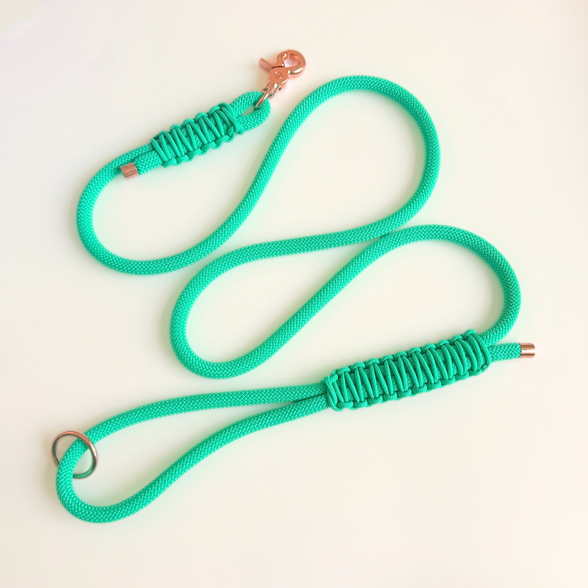 A bright mint green paracord dog leash with a rose gold metal clasp and metal ring, laid out on a clean off-white background.