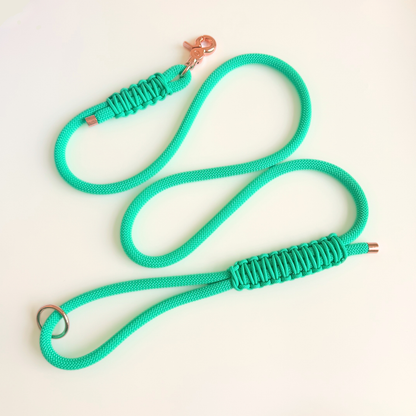 A bright mint green paracord dog leash with a rose gold metal clasp and metal ring, laid out on a clean off-white background.