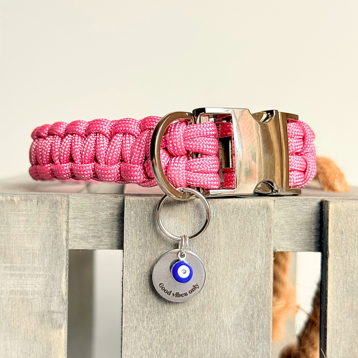 Silver plated brass and stainless steel 15mm dog collar charm with ID tag. Personalised custom identification tag with a small, blue Turkish Evil Eye charm, on a 15mm silver split ring. Engraved with the words ‘Good vibes only’ on the front. Pictured attached to a pink paracord dog collar.