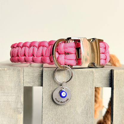Silver plated brass and stainless steel 15mm dog collar charm with ID tag. Personalised custom identification tag with a small, blue Turkish Evil Eye charm, on a 15mm silver split ring. Engraved with the words ‘Good vibes only’ on the front. Pictured attached to a pink paracord dog collar.