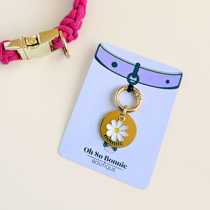 Gold white daisy flower dog collar ID tag, Enamel floral charm with dog name and address details. easily clips onto collar or harness.  Pictured on the display card, next to a pink paracord dog collar.
