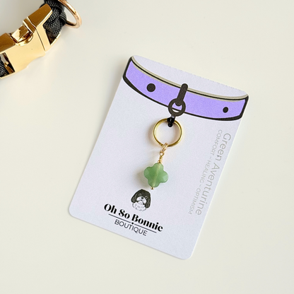 Green aventurine four leaf clover shaped crystal dog collar charm. Crystals for dogs, gemstone for optimism, healing and comfort. Pictured on the display card, next to a black paracord dog collar.