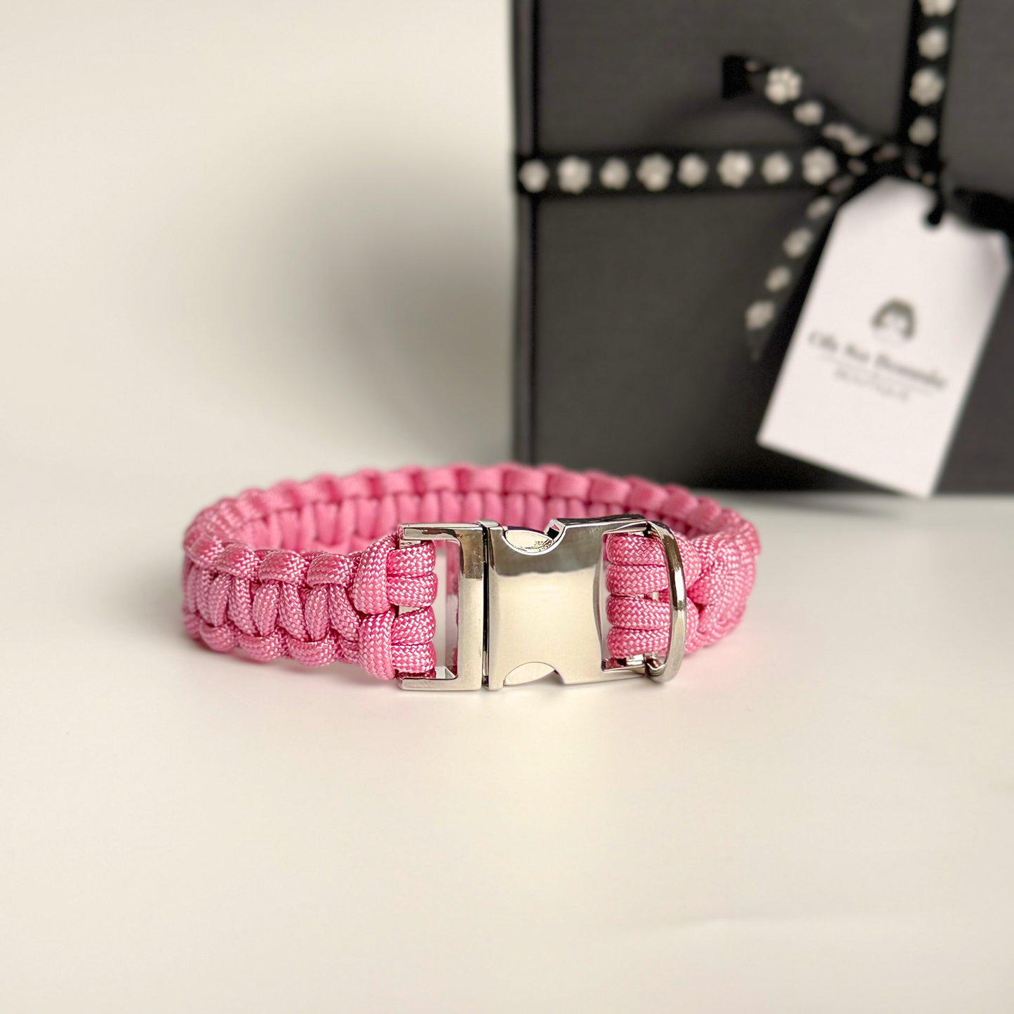 ‘Lavender pink’ handmade paracord dog collar with silver coloured buckle clasp. Custom made to your required size. Braided macrame style pet neckwear. Pictured in front of the gift box.