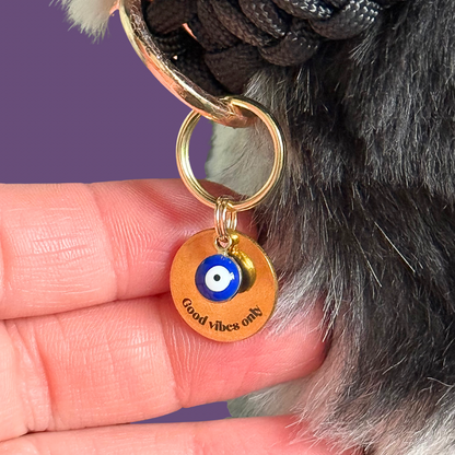Gold plated brass and stainless steel 15mm dog collar charm with ID tag. Personalised custom identification tag with a small, blue Turkish Evil Eye charm, on a 15mm brass split ring. Engraved with the words ‘Good vibes only’ on the front. Pictured close up.