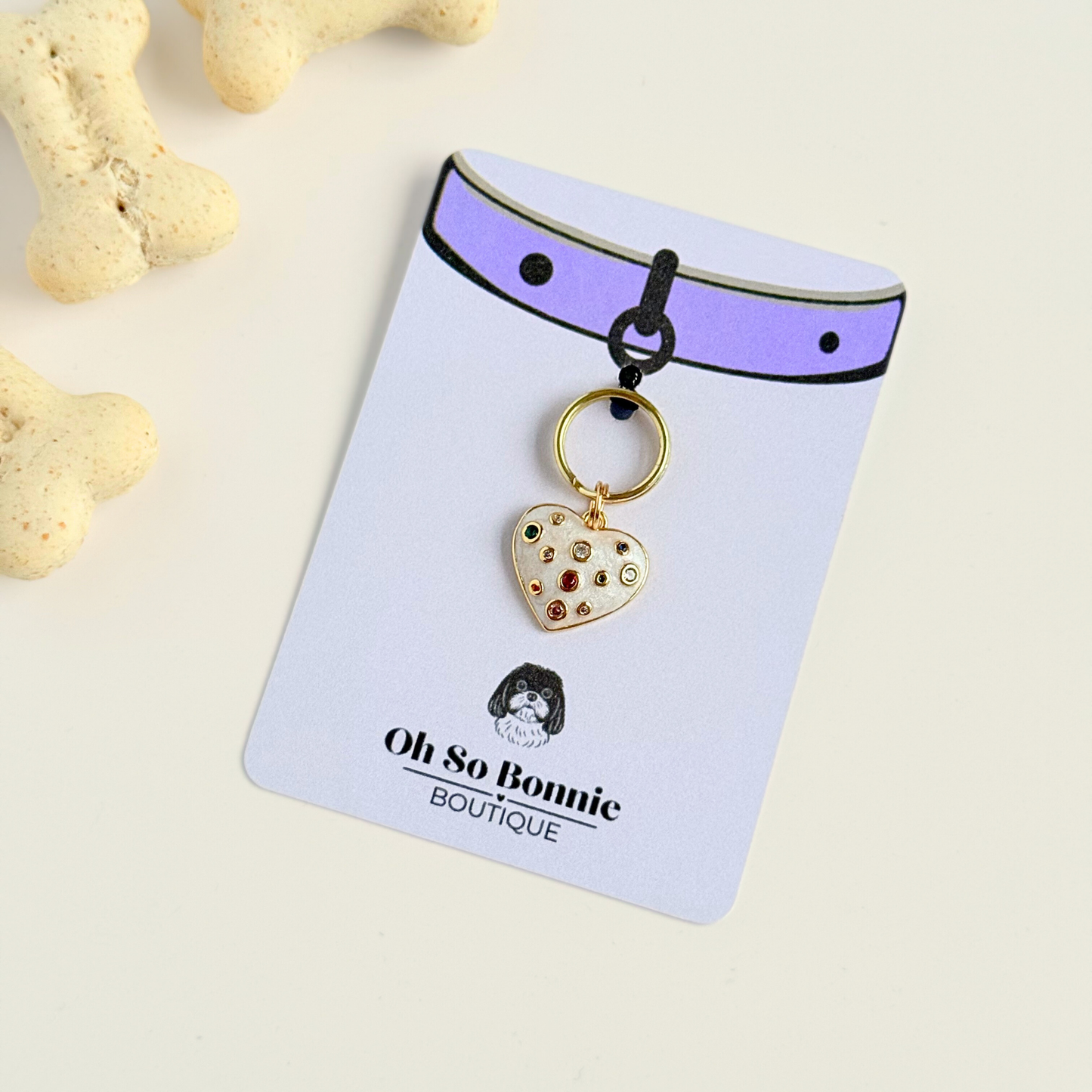Heart shaped cream / off white pearlescent coloured enamel and brass pet collar charm featuring a selection of multicoloured cubic zirconia stones. Pictured on the display card.