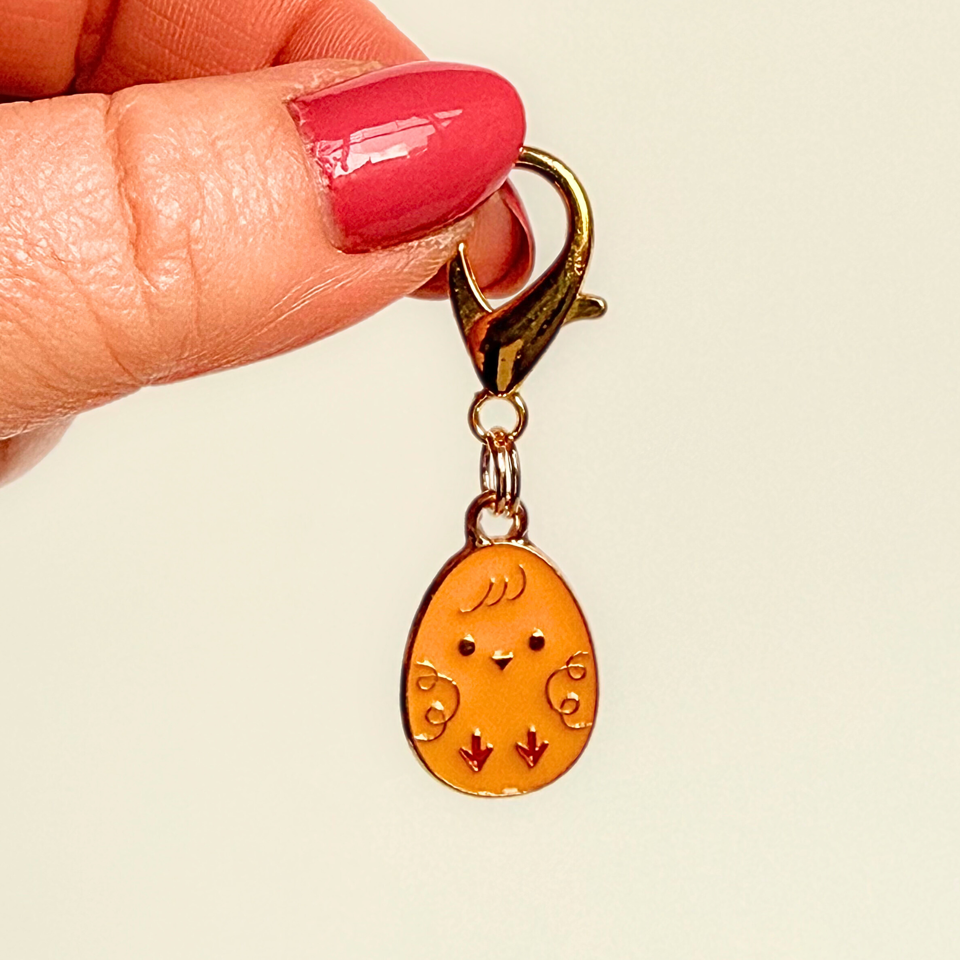 Yellow chick Easter egg enamel dog collar charm that easily attaches to collars and harnesses with a gold plated lobster clasp. Pictured being held against a cream background.￼