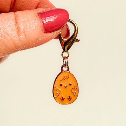 Yellow chick Easter egg enamel dog collar charm that easily attaches to collars and harnesses with a gold plated lobster clasp. Pictured being held against a cream background.￼