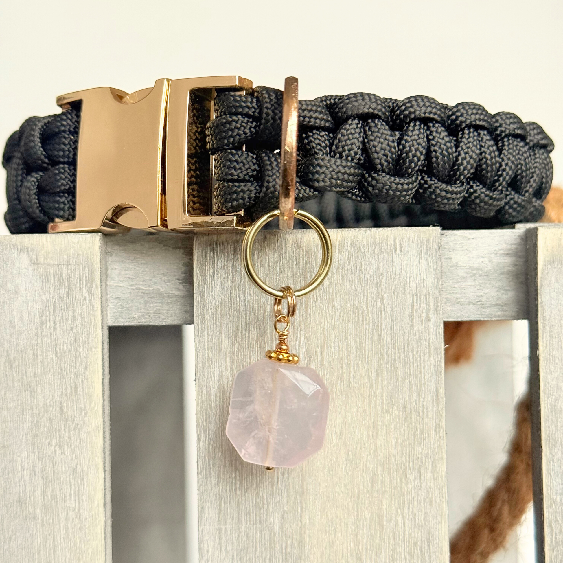 Handmade dog collar charm featuring a 17mm pink rose quartz natural gemstone faceted square crystal bead. Hung on a gold plated brass split ring with a daisy gold spacer bead that attaches onto your pet collar. Rose quartz can help pets with love, comfort and calming. Close up picture attached to a black paracord dog collar.