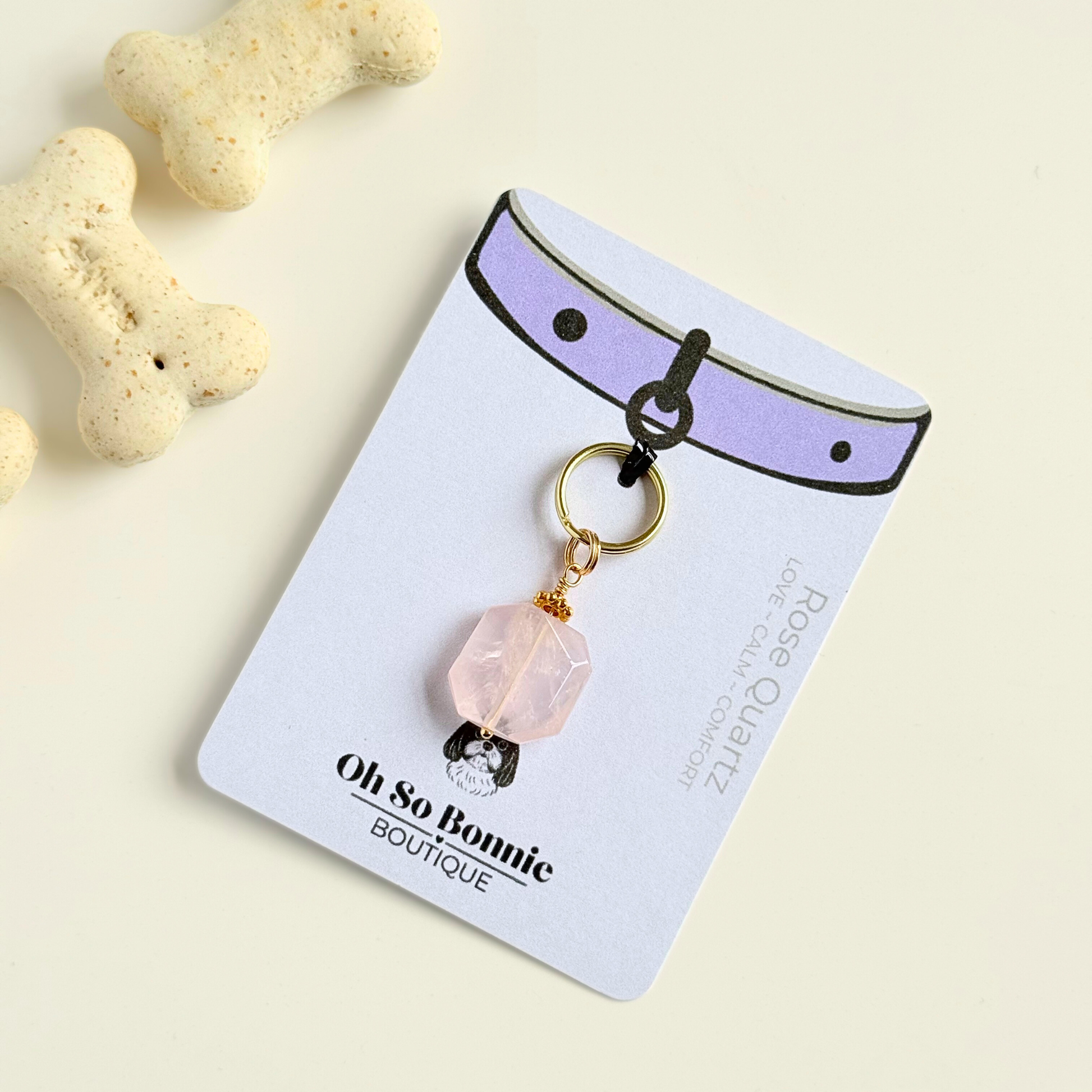Handmade dog collar charm featuring a 17mm pink rose quartz natural gemstone faceted square crystal bead. Hung on a gold plated brass split ring with a daisy gold spacer bead that attaches onto your pet collar. Rose quartz can help pets with love, comfort and calming. Pictured on the display card, next to some dog biscuits.
