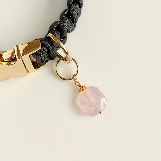 Handmade dog collar charm featuring a 17mm pink rose quartz natural gemstone faceted square crystal bead. Hung on a gold plated brass split ring with a daisy gold spacer bead that attaches onto your pet collar. Rose quartz can help pets with love, comfort and calming. Pictured attached to a black paracord dog collar.