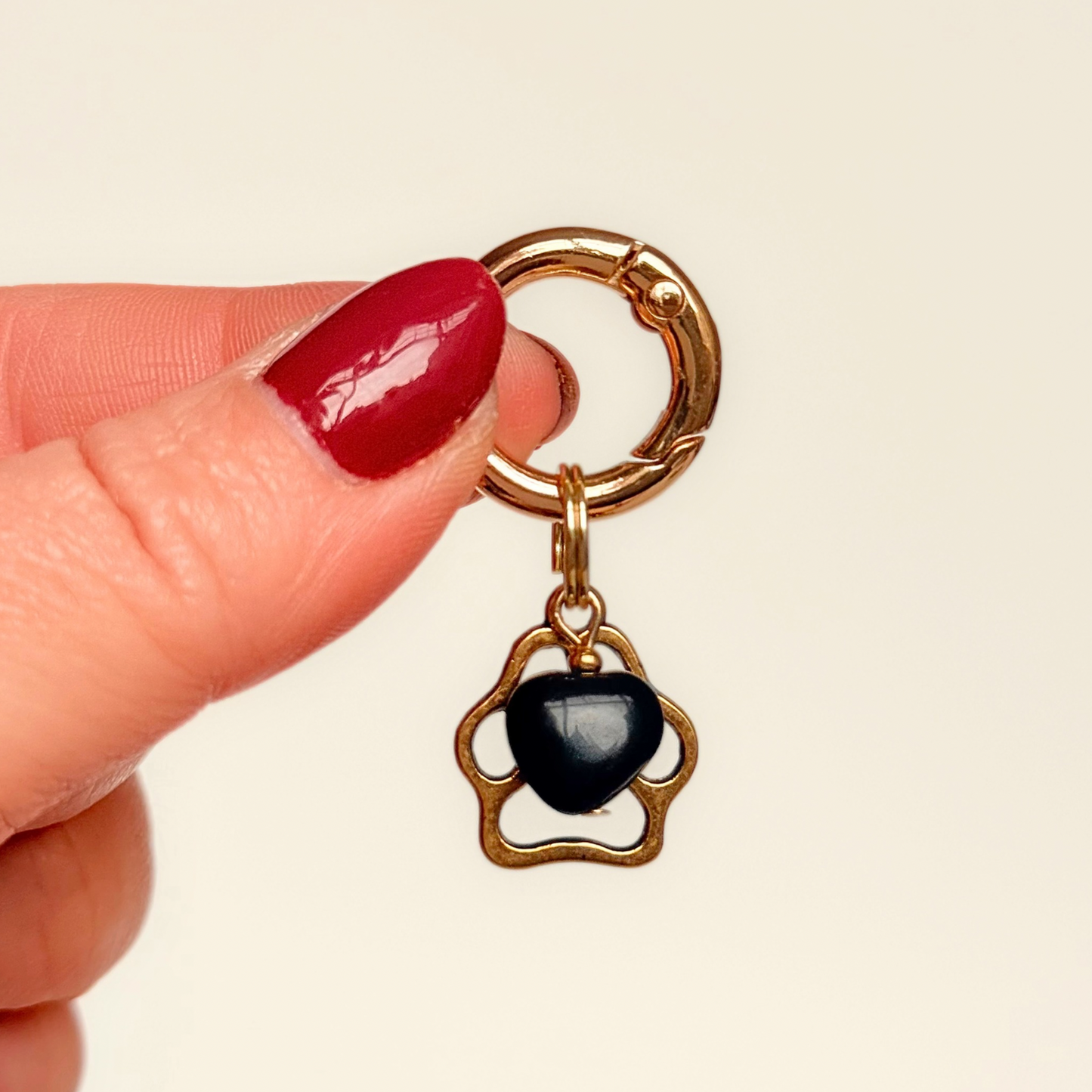 Crystal for dogs pet collar charm featuring a 10mm black onyx heart shaped bead and a brass gold coloured paw print tag. A stone for protection, strength and stability. Pictured being held against a cream background