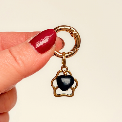 Crystal for dogs pet collar charm featuring a 10mm black onyx heart shaped bead and a brass gold coloured paw print tag. A stone for protection, strength and stability. Pictured being held against a cream background