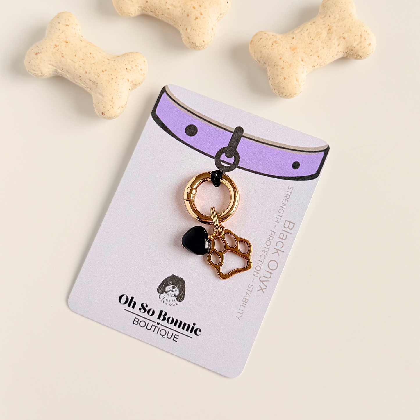 Crystal for dogs pet collar charm featuring a 10mm black onyx heart shaped bead and a brass gold coloured paw print tag. A stone for protection, strength and stability. Pictured on the display card, next to some dog biscuits 