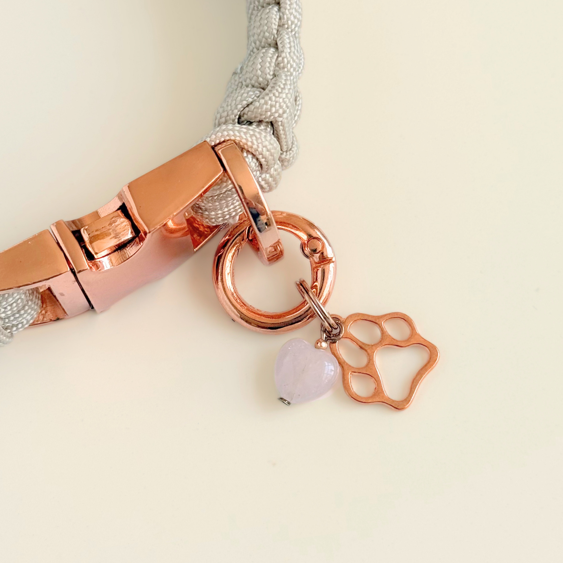 Crystal for dogs pet collar charm featuring a 10mm rose quartz heart shaped bead and a brass rose-gold coloured paw print tag. A stone for love, calm and comfort. Pictured attached to a pearl rose paracord dog collar against a cream background.